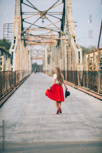 stylish portrait of a beautiful young woman on the bridge in a red skirt and black hat on a sunny day at sunset posing and smiling Life Style