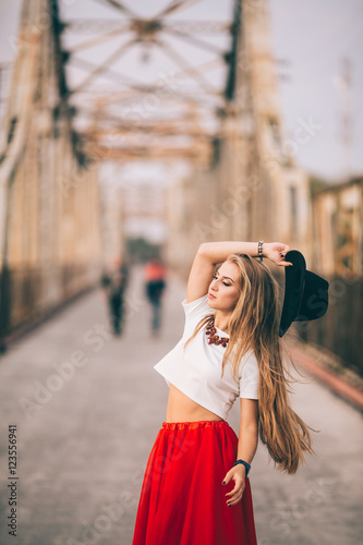 stylish portrait of a beautiful young woman on the bridge in a red skirt and black hat on a sunny day at sunset posing and smiling Life Style
