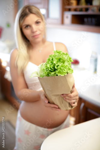 pregnant woman holding paper bag with leaves salad