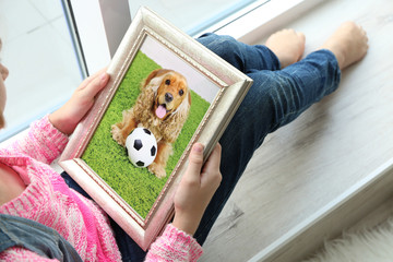 Little girl holding photo frame with picture of dog. Happy memories concept.