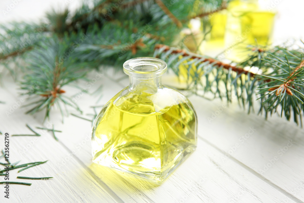 Bottle of coniferous essential oil and branches on wooden background, close up view Bottle of coniferous essential oil and branches on wooden background, close up view