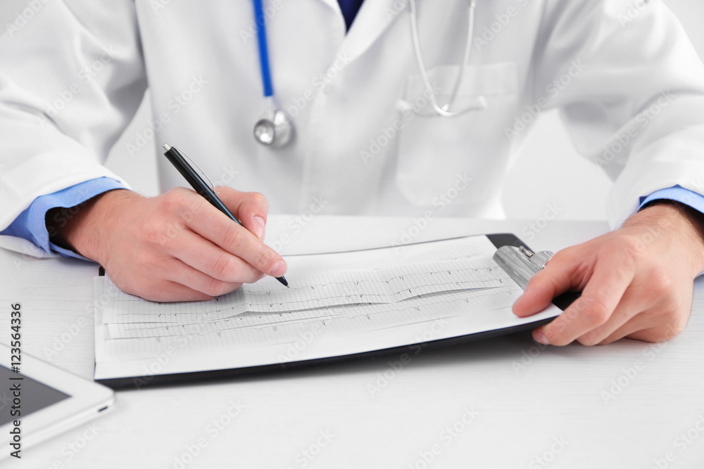 Fototapeta premium Male doctor making notes on cardiogram, close up view