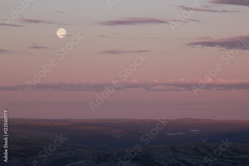 Soft pink sunset sky over mountain valley with full moon. Arctic summer, the tundra, Norway.