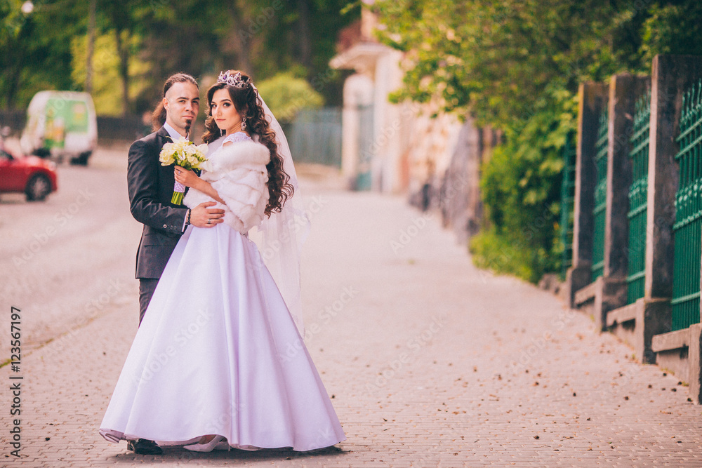 gorgeous wedding couple walking in the old city.  Man with long hair and piercing. Woman in beautiful gemstone crystal crown.