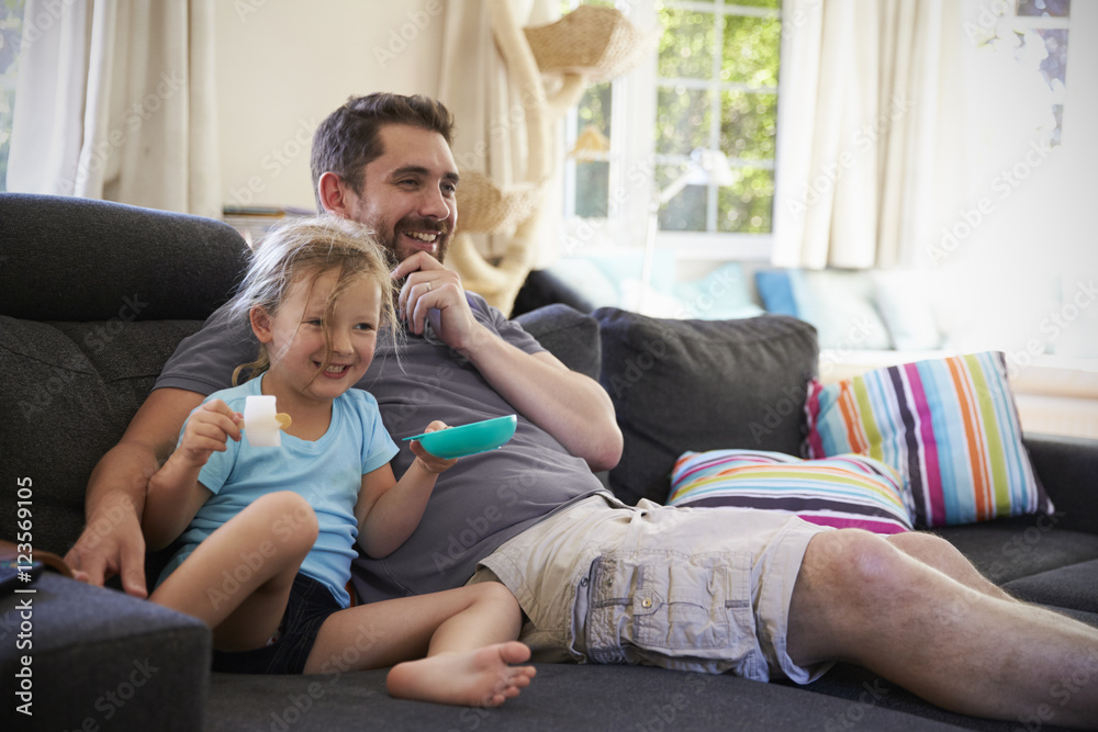 Father And Daughter Sitting On Sofa Watching TV Together Father And Daughter Sitting On Sofa Watching TV Together