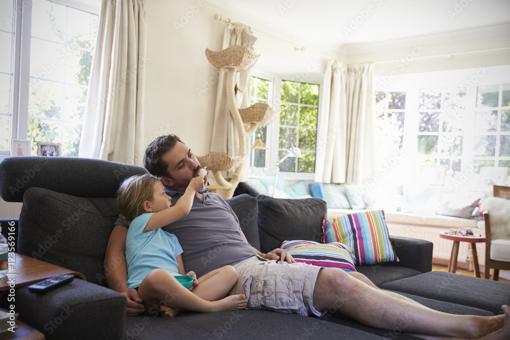 Father And Daughter Sitting On Sofa Watching TV Together Father And Daughter Sitting On Sofa Watching TV Together