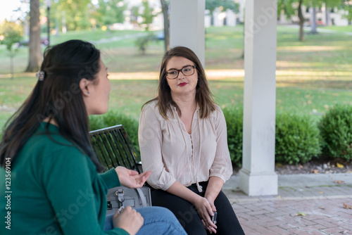 College aged girls having a conversation on a bench in a park