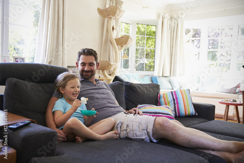 Father And Daughter Sitting On Sofa Watching TV Together