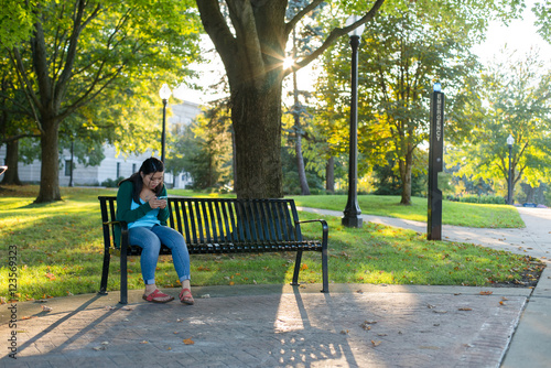 College girl sitting on bench in park using her mobile device