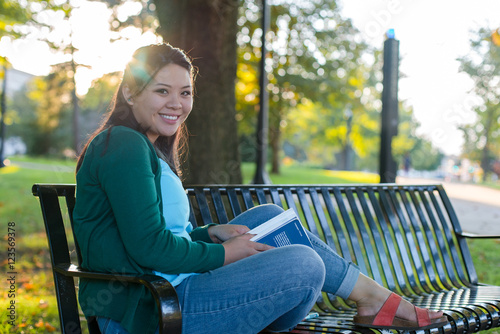College aged girl smiling and studying on a bench in a park