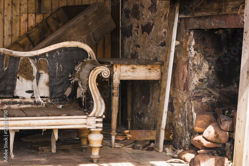 A landscape image of the inside of a derelict croft showing a Chaise Longue and the fireplace. photo