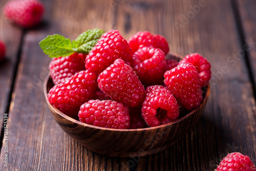 Ripe sweet raspberries in bowl on wooden table.