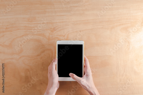 Top view of Male hands holdind tablet touch computer gadget on wooden table background.