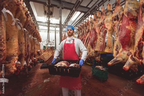 Butcher carrying crate of red meat in storage room photo