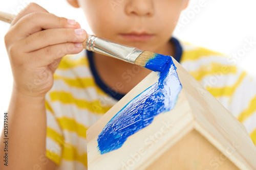 Child paints wooden birdhouse on a white background