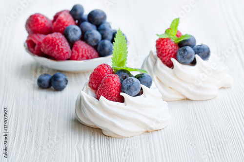 Mini Pavlova meringue cakes with berries and mint on white wood