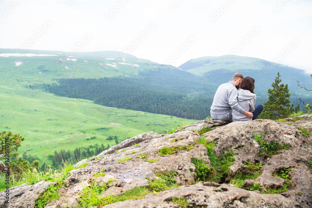 Loving young hipster couple sitting on a mountain, hugging and l Loving young hipster couple sitting on a mountain, hugging and l