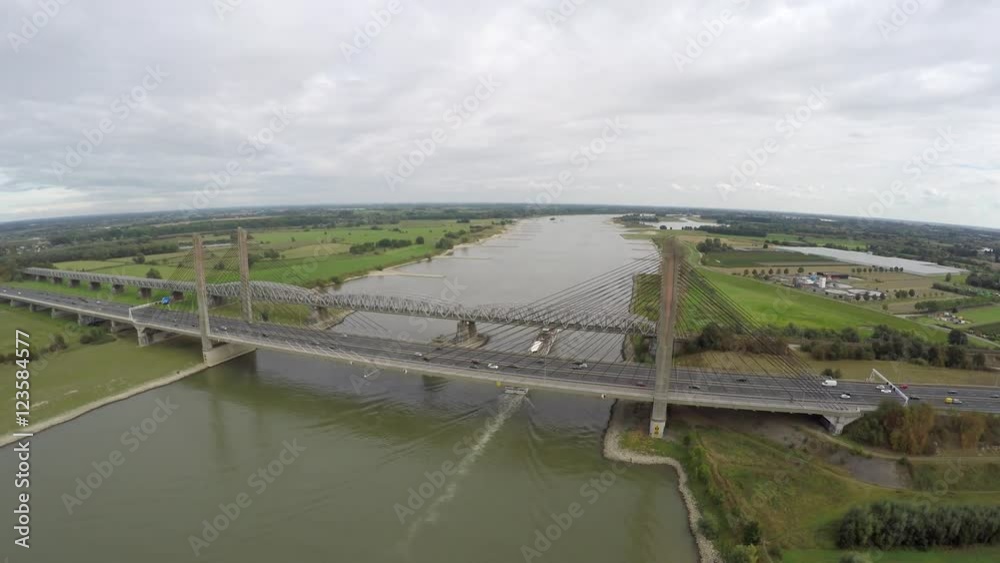 Aerial drone moving away from briges with traffic moving over and barge transport ship moving underneath it on the cable-stayed bridge highway is running over on smaller bridge railroad over river 4k Aerial drone moving away from briges with traffic moving over and barge transport ship moving underneath it on the cable-stayed bridge highway is running over on smaller bridge railroad over river 4k