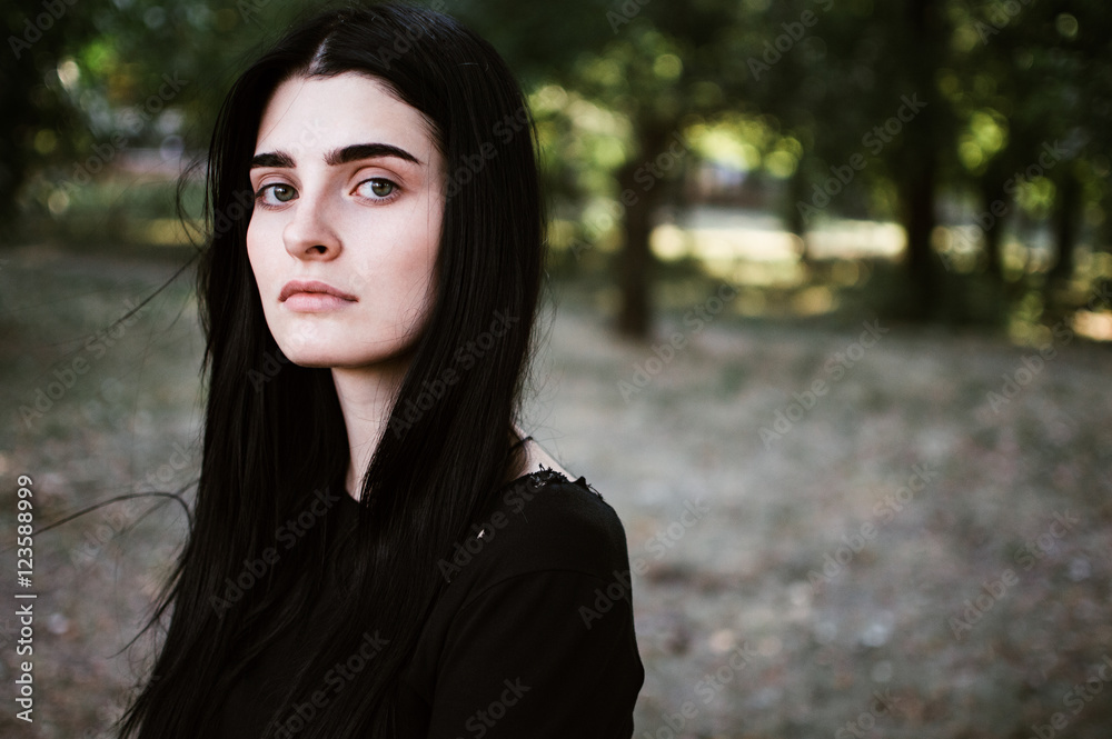 Outdoors portrait of beautiful young brunette woman looking at camera
