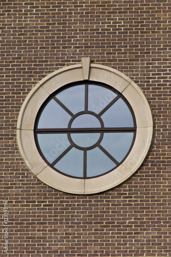Portal style window on brick wall with clear blue sky reflected in window.