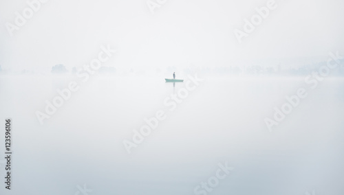 Alone fisherman on the boat in a thick fog on the lake on an autumn morning in calm weather photo
