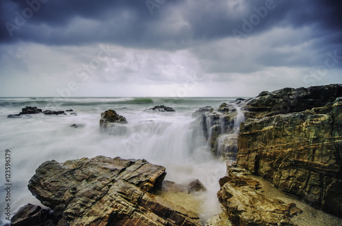 beautiful beach with rock hitting by waves. soft focus due to long exposure. dramatic dark clouds and rocky island © amirul syaidi