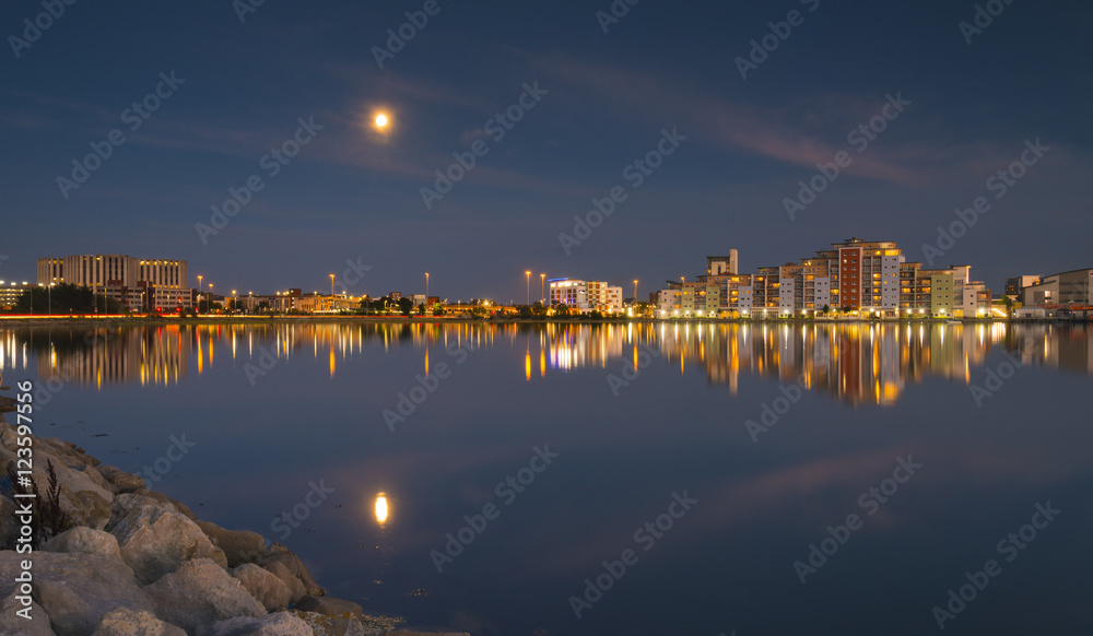The moon and cityscape lights, reflect off harbour waters, poole
