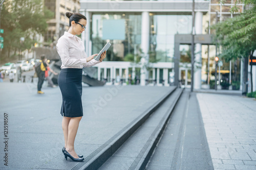 Professional business woman in white shirt and black skirt using modern tablet while working on new project outdoors, Business woman standing on the square and using modern tablet, blurred background