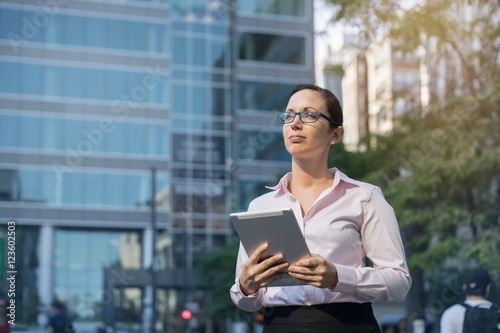 Portrait of young attractive businesswoman with modern tablet outdoors, close-up of smiling businesswoman in white shirt outdoors near her office, Woman working outdoor, sunny day, blurred background