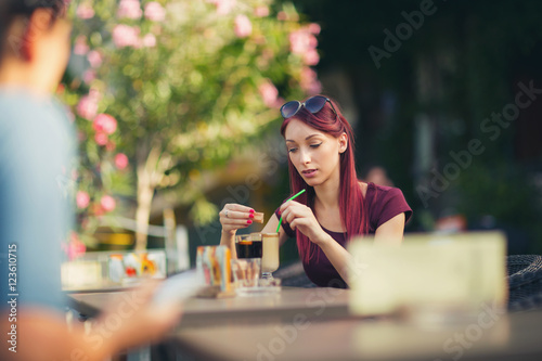 Young beautiful red hair woman drinking coffee in summer cafe ou