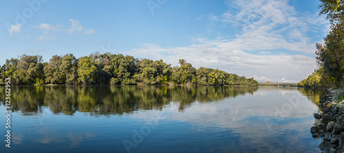 Early autumn landscape panorama with the river and a locomotive crossing the railway bridge .