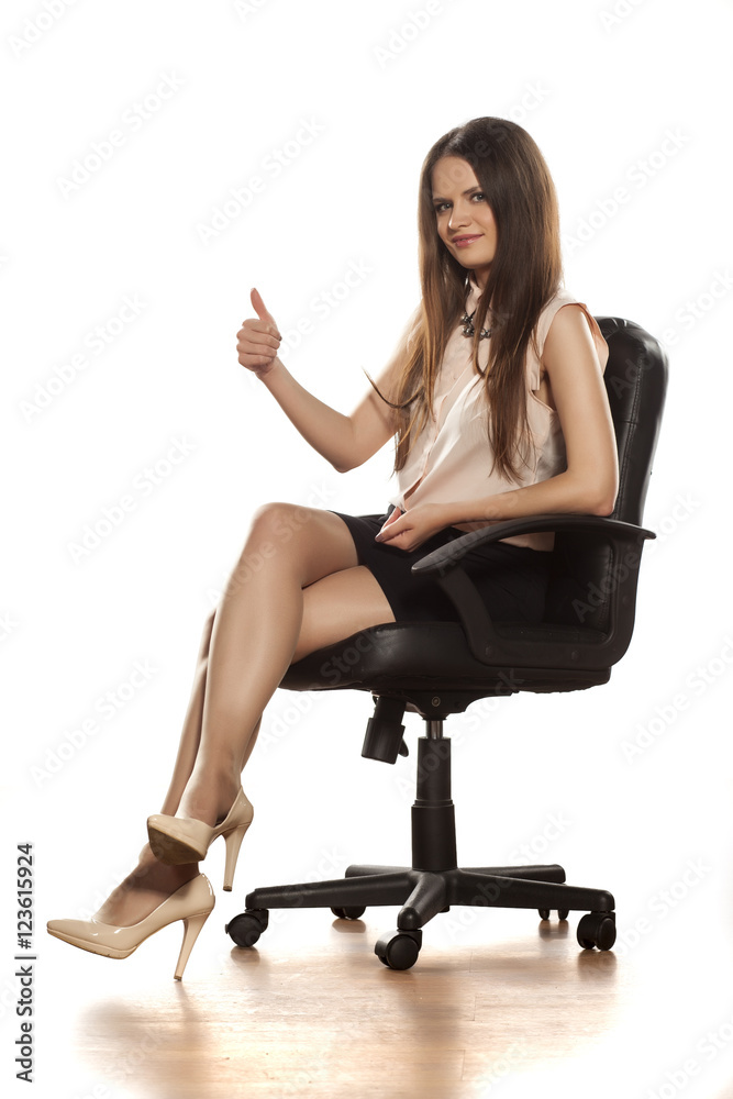 Young business woman sits a leather chair with legs crossed and showing thumbs up Young business woman sits a leather chair with legs crossed and showing thumbs up