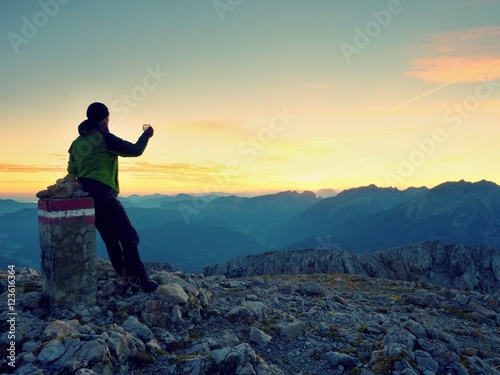 Hiker takes selfie photo. Man  sit on Austria Germany border stone on Alpine mountain. © rdonar