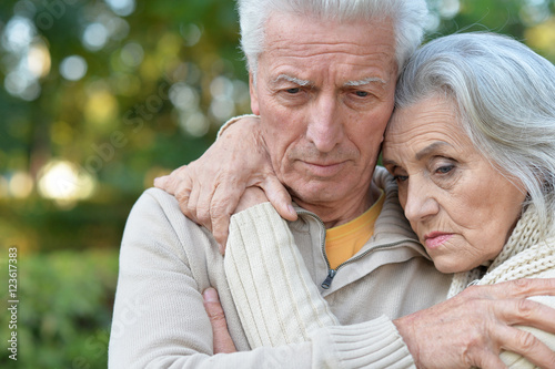 Sad elderly couple standing embracing outdoors