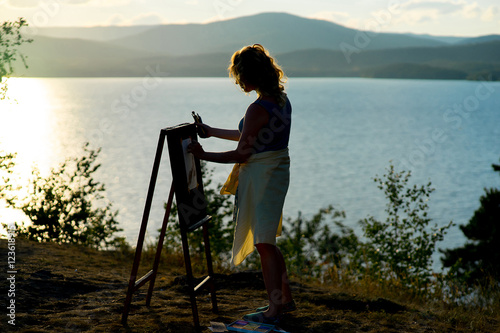 young artist draws a seascape at sunset