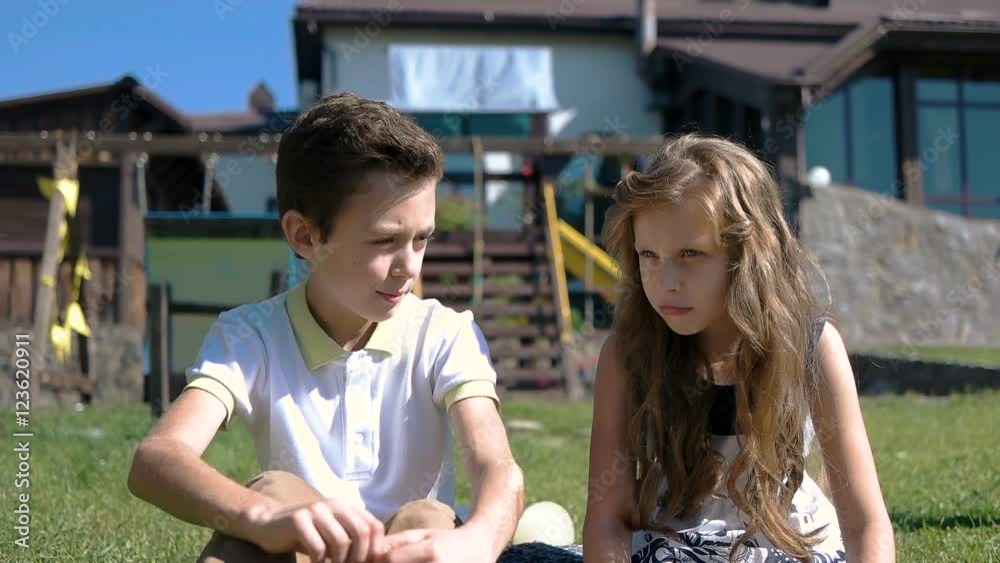 Smiling boy and girl sit on grass near flower garden Smiling boy and girl sit on grass near flower garden