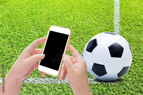 Hand holding smartphone with soccer ball on play fields photo