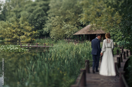 Bride and groom walk  along a wooden path through the rushy bog