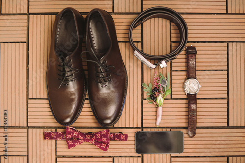 set of groom shoes, bow tie, watch, belt and boutonniere lie on the background of wooden floor