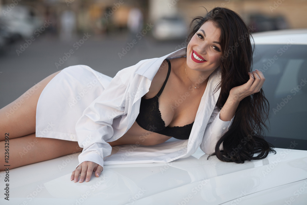 Naklejka premium Young sexy brunette woman in black lingerie and white shirt on sport car hood.
