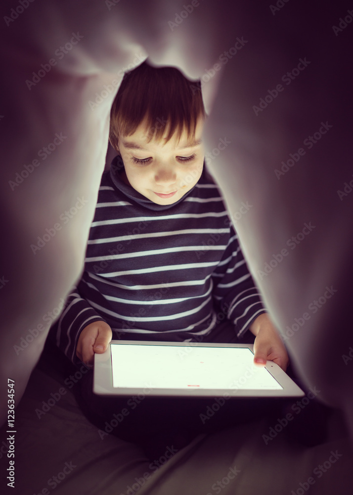 Cute little boy alone with tablet computer under blanket at nigh Cute little boy alone with tablet computer under blanket at nigh
