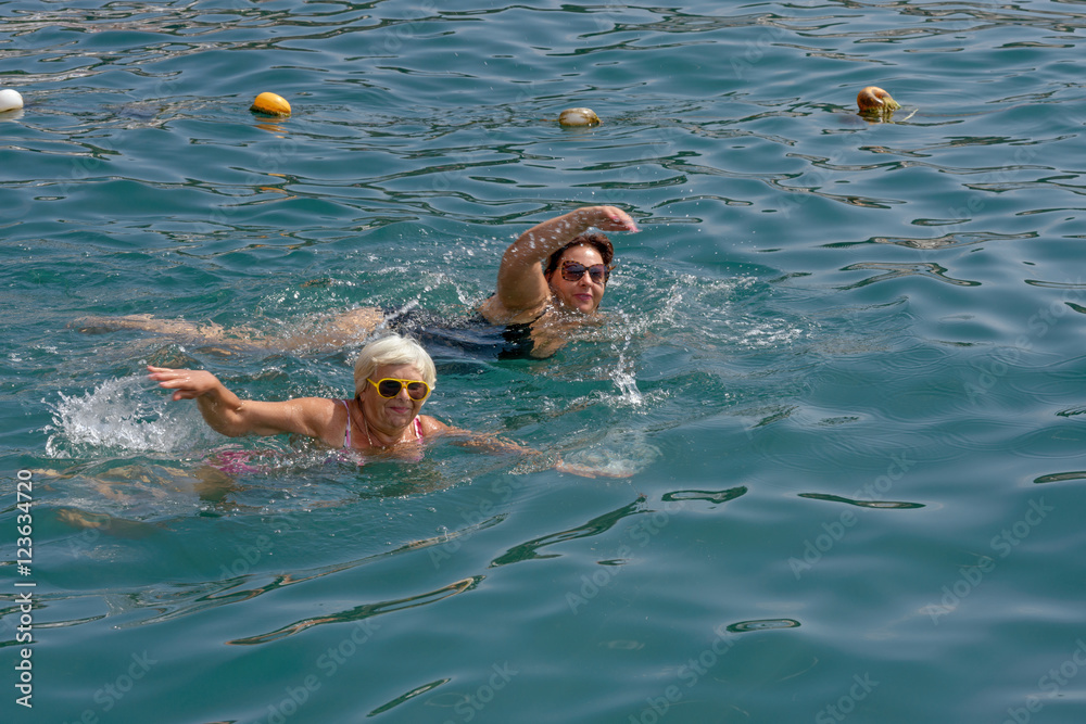 Two women are swimming in clear water of sea.