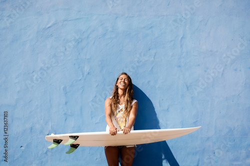 happy surfer girl with surfboard in front of blue wall photo