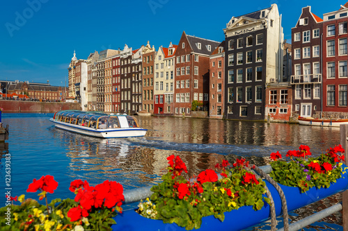 Photography Beautiful typical Dutch dancing houses and tourist boats at the Amsterdam canal Damrak in sunny day, Holland, Netherlands