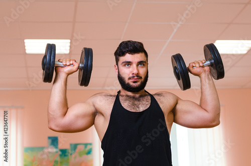 Handsome young muscular man exercising with dumbbells.