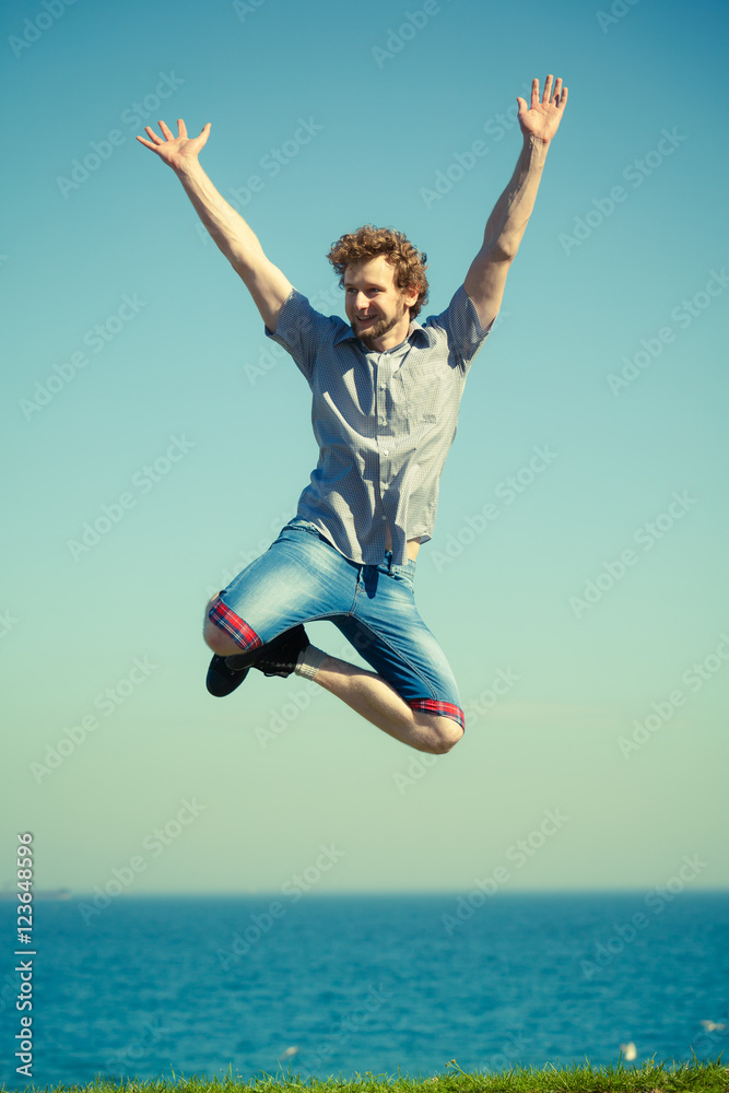 Carefree man jumping by sea ocean water.