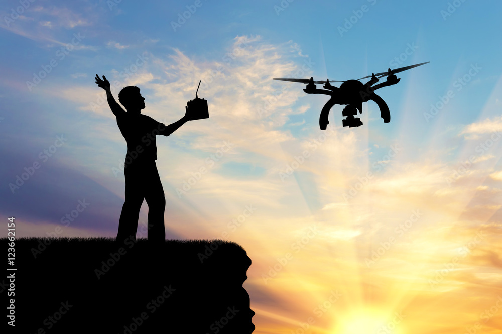 Silhouette of a flying drone, and a man with a remote control on the mountain Silhouette of a flying drone, and a man with a remote control on the mountain