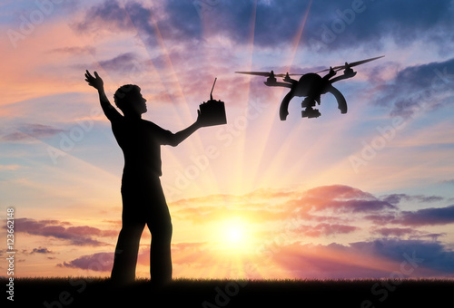 Silhouette of a flying drone, and a man with a remote control at sunset.