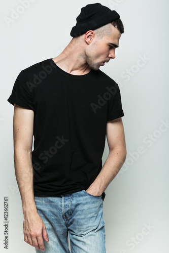 Close up portrait of stylish brutal guy keeping hand in pocket while posing in studio on grey background. Copyspace. 
