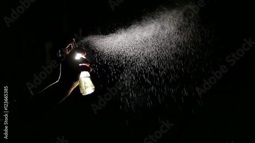 Beautiful woman's hand sprays perfume In the air. Black background. photo